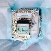 a boxed gift with a small candle with a label that has a blue watercolor design with the phrase "oh boy!" in calligraphy on the front. Also in the box is a single-use bag of lavender bath salts and vanilla mint lip balm. These gifts make great prizes for baby shower games or gender reveal gifts for grandparents and pampering gifts for new moms!